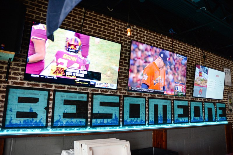 Inside Cobo's — the games on TVs above the BE SOMEONE sign